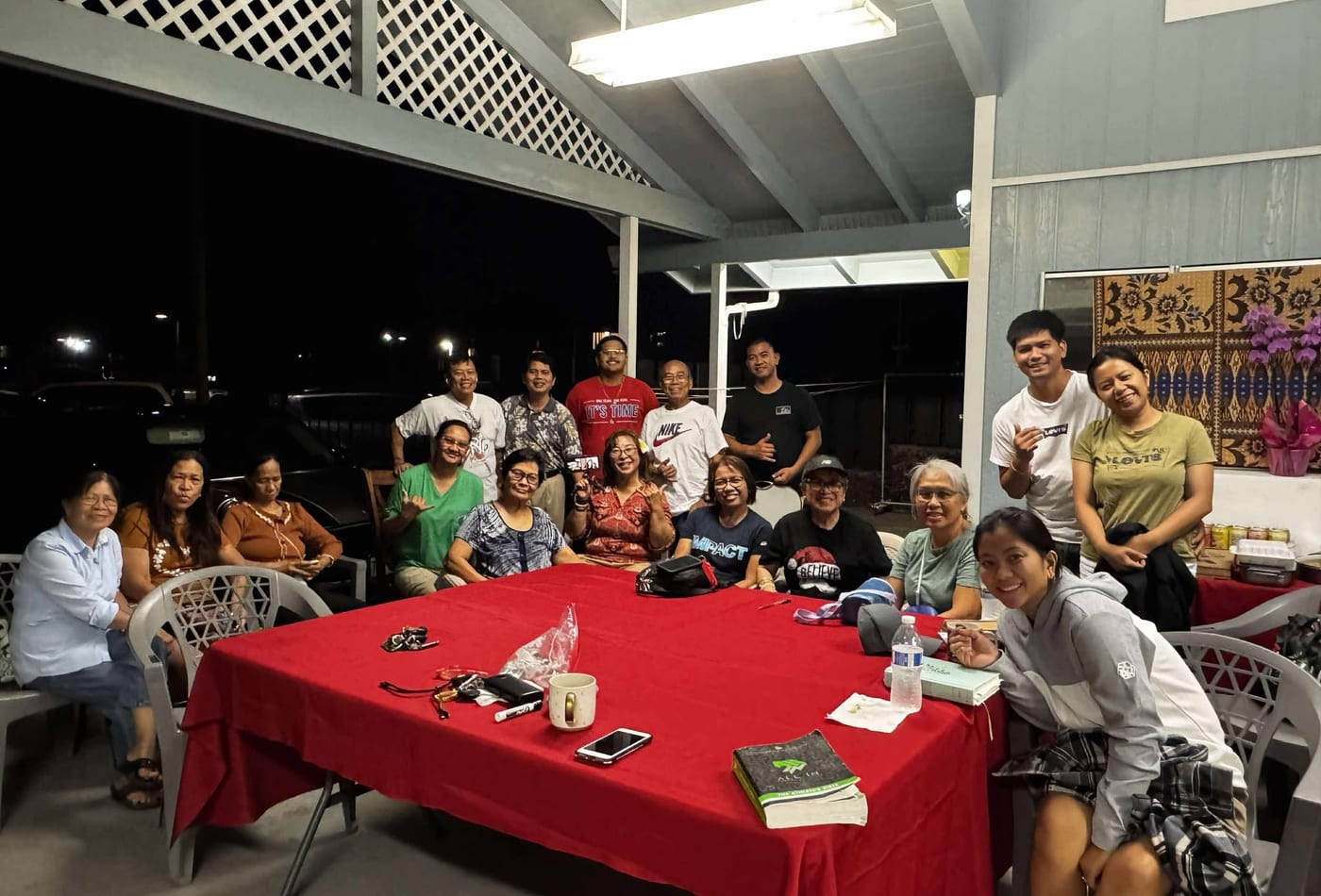 Bible study group gathered around a red table in the covered lanai at night