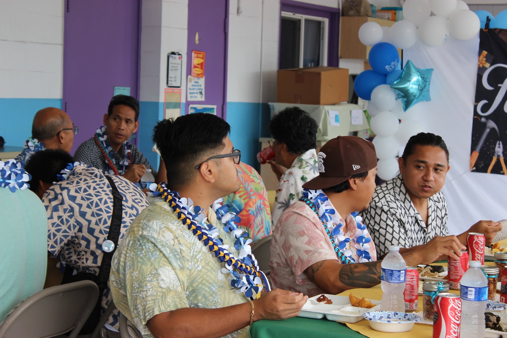 Men wearing leis seated together at the fellowship table