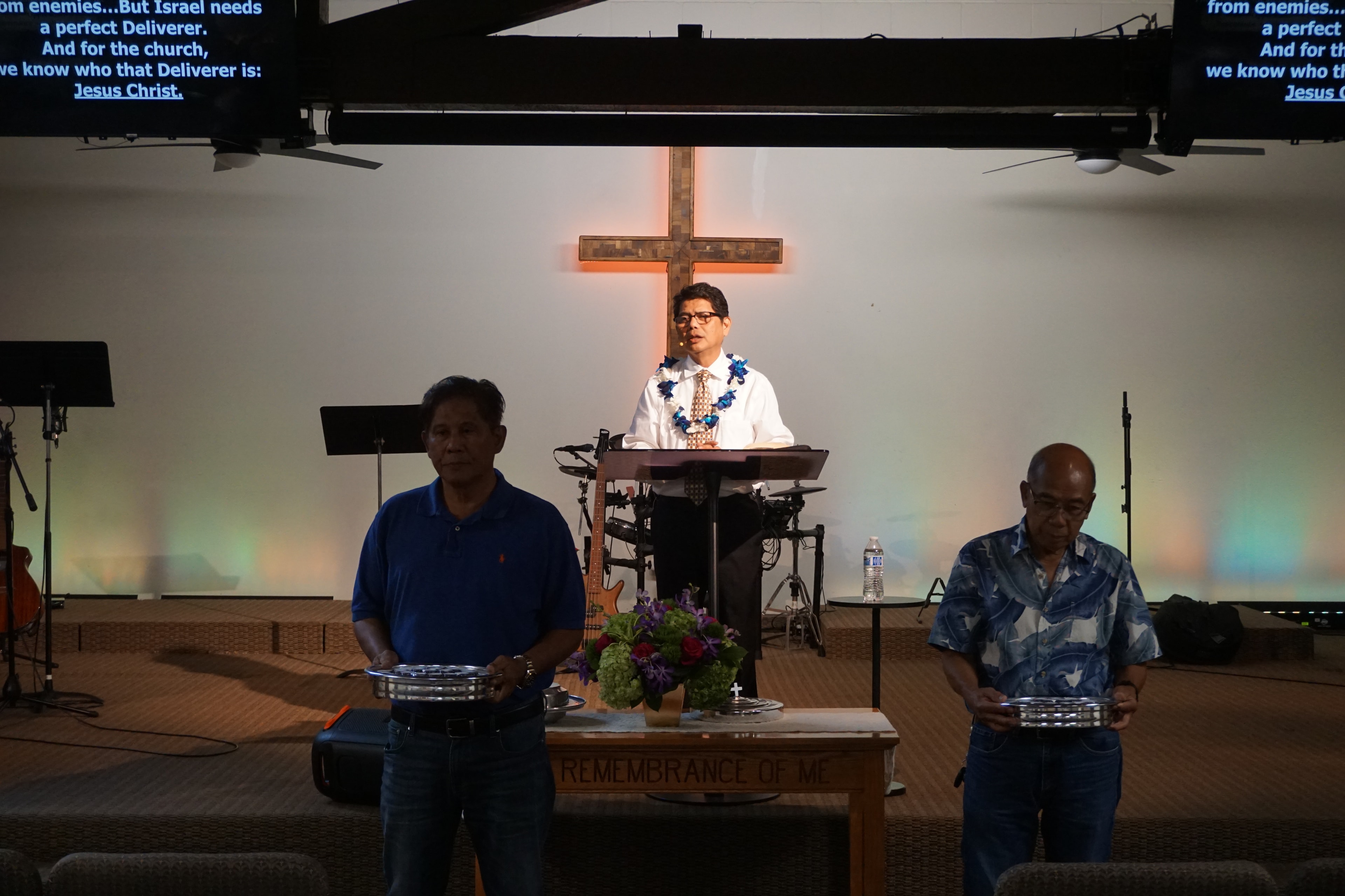 Pastor preaching with deacons holding offering plates