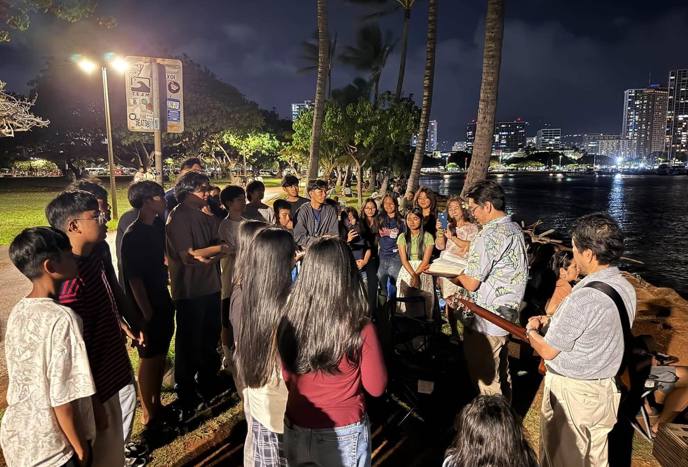 Youth gathered by the waterfront at night for an outdoor ministry event